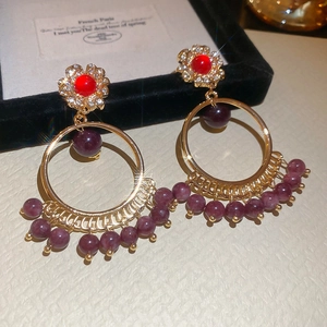 Detail of vintage style gold hoop earrings with red stones and purple beaded tassels