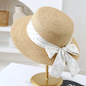 Détail d'un chapeau de paille avec un ruban à pois noirs sur un support en métal doré
