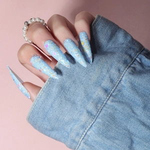 Close-up of long stiletto press-on nails in light blue with iridescent glitter and sequins