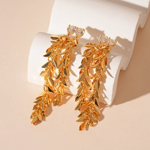 Detail of gold tassel earrings with leaf charms and a sparkling heart-shaped zircon stone