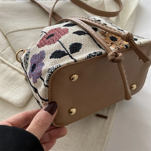 Ethnic style floral bucket bag featuring woven fabric, leather base and gold metal feet