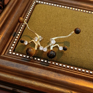 Makro-Detail von unregelmäßigen Goldohrringen mit Tigerauge-Stein und Zirkonia-Steinen