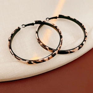 Close-up of leopard print hoop earrings on a textured neutral background with soft lighting