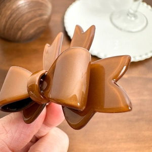 Elegant brown acetate double bow hair clip held by hand over a wooden tabletop