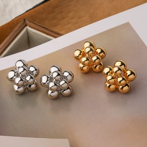 Polished flower stud earrings in gold and silver finish on a neutral paper background