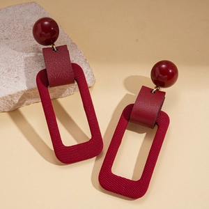 Detailed close-up of dark red geometric resin earrings with leather and fabric texture