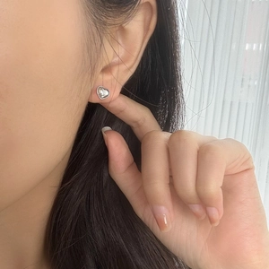 Close-up of heart-shaped silver stud earring on ear with polished mirror finish