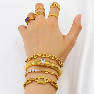 Close-up of layered gold bracelets and rings with purple zircon stones on white fabric
