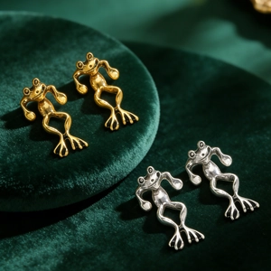 Macro shot of vintage gold and silver frog stud earrings on premium green velvet display