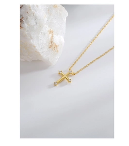 Close-up of a gold cross pendant with zircon stones on a white textured stone surface