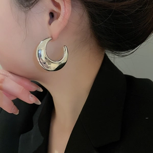 Close-up of a model wearing large silver C-shape hoop earrings with high-polish mirror finish