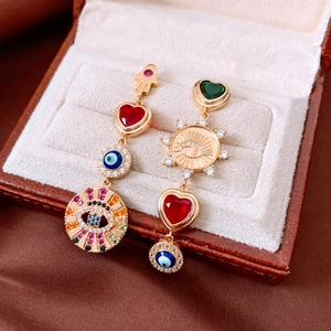 Detail of asymmetric gold earrings with Evil Eye, Fatima Hand and heart charms