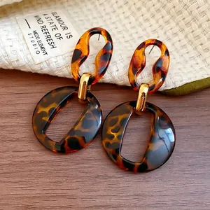 Fashionable tortoiseshell resin hoop earrings with gold metal links on a neutral fabric