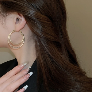 Detail of gold double-layered hoop earrings with smooth and twisted textures on model