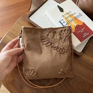 Détail macro d'un sac bandoulière en daim marron foncé avec broderies florales élégantes