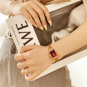 Detail of vintage square red dial watch with gold mesh band on wrist with rings