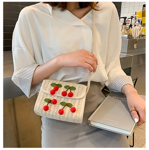 Detail of a straw crossbody bag with 3D cherry accents and woven shoulder strap