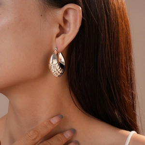 Close-up of a model wearing a large gold geometric earring with unique mesh texture