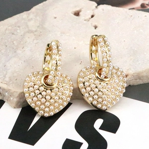 Close-up of gold heart hoop earrings with white pearls on a natural stone surface