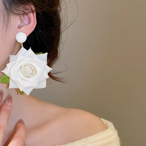 Close-up of oversized white fabric rose earrings with green leaves on model