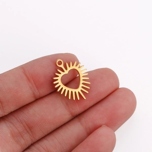 Detail view of a gold heart pendant with radial sunburst pattern held in hand for scale