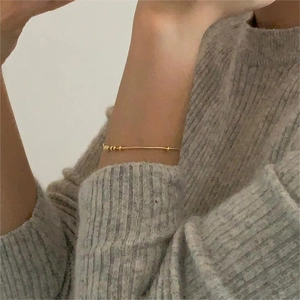 Close-up of minimalist gold beaded snake chain bracelet worn on a wrist with a sweater