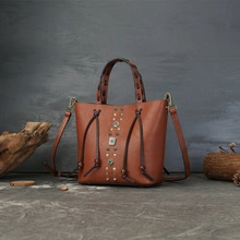 Nahaufnahme der braunen Lederbeuteltasche mit Nieten und geflochtenem Henkel im Detail.