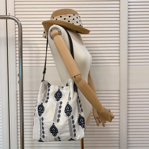 Detailed view of ethnic plant embroidery on a white linen tote bag shown on a mannequin