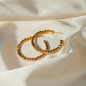 Gros plan de créoles plaquées or 18k avec cristaux sur un tissu en soie de luxe