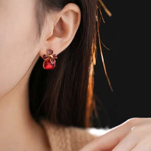 Close-up of vintage earrings with red enamel flowers and square red gemstone on ear