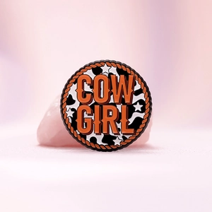 Retro Cowgirl enamel pin with cow print pattern and orange rope border design