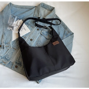 Detail of black nylon hobo bag with leather logo tag next to a denim jacket and book