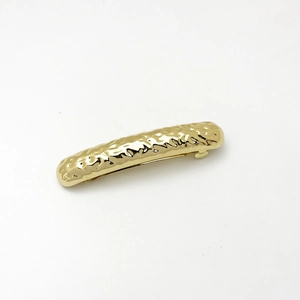 Macro view of golden hair clip with hammer texture finish and curved metallic design