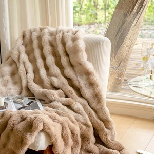 Detailed view of beige wavy faux fur blanket draped over a white chair in a bright room