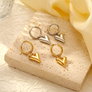 Two pairs of heart pendant hoop earrings in gold and silver finish on stone background