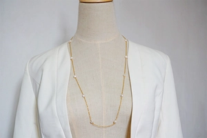 Detailed view of a long layered freshwater pearl necklace on a white suit jacket