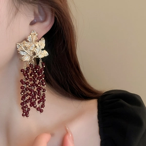 Close-up of vintage gold leaf earrings with dark red beaded tassels on a model