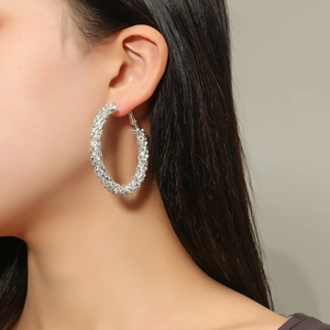 Macro shot of oversized silver hoop earrings with shimmering crystals on a model