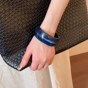 Detail of dark blue translucent acrylic chunky resin bangle worn on wrist with woven bag