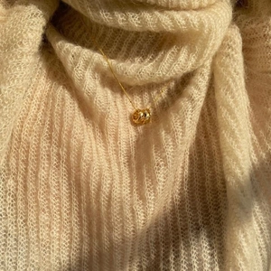 Detailed view of tricolor interlocking rings pendant on soft beige knitwear background