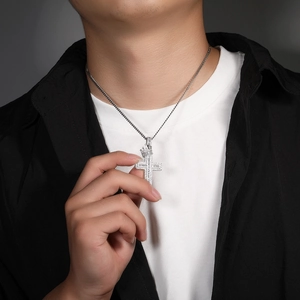 Detail of silver crown cross pendant with cubic zirconia worn by a male model