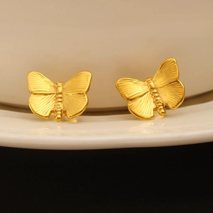Macro shot of 18K gold-plated stainless steel butterfly stud earrings on a ceramic dish