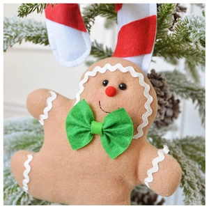 Detailed close-up of a plush gingerbread man ornament with green bow on a Christmas tree