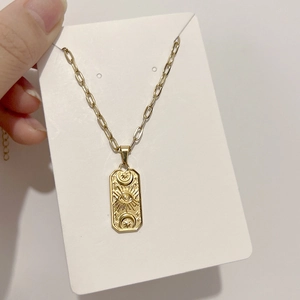 Macro detail of gold-plated paperclip chain with rectangular evil eye engraved pendant