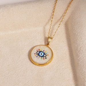 Detail of gold evil eye pendant necklace with blue eye inlay on beige velvet base