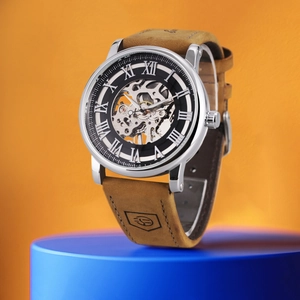 Detail of mechanical watch with skeleton dial on a blue pedestal against orange background