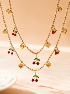 Détail d'un collier multicouche doré avec pendentifs cerise, cœur et fraise