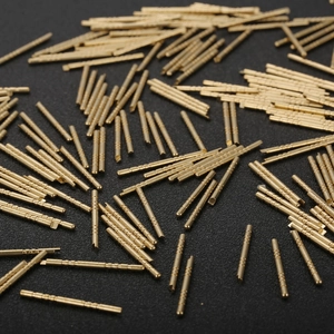 Bulk gold metal connector pins with textured circular grooves on black background