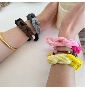 Close-up of colorful braided elastic hair ties in brown, pink and yellow on model wrist