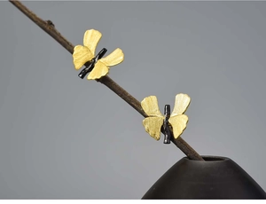 Artistic detail of gold ginkgo leaf earrings with brushed metal finish on wood branch
